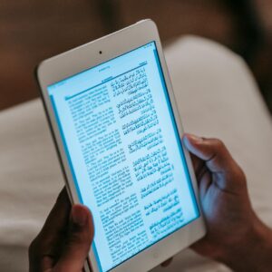 Crop unrecognizable person in casual clothes reading text on tablet against blurred background in room